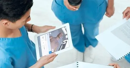 two nurses viewing a tablet displaying a simulated patient
